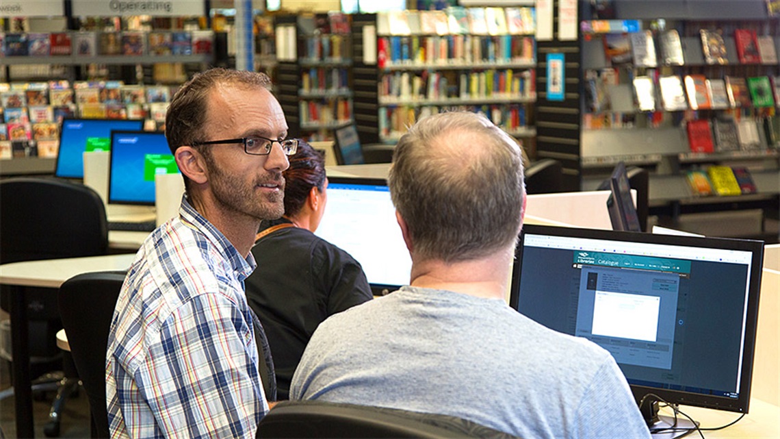 A librarian helping a customer on the public computer in a library. 