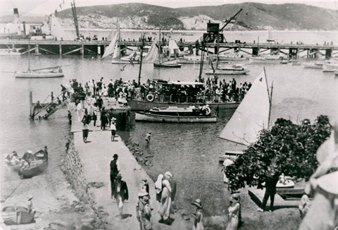 Photograph of Onerahi waterfront taken early 20th century showing jetty, wharf, various boats and Limestone Island in the background. 