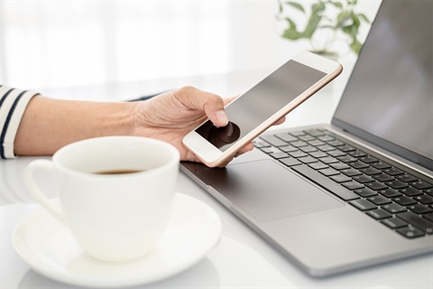 A person using their phone with a cup of tea in the frame. 