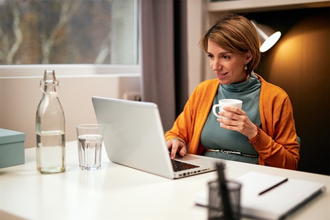 Woman drinking a cup of tea while checking her laptop. 