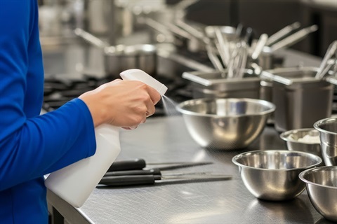 A person is cleaning a commercial kitchen with a spray bottle. 