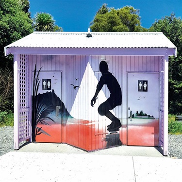 Photo of the front of the Parua Bay Community Centre public toilet block mural: a skateboarder launches across the front wall, with Mount Manaia standing tall behind them. 