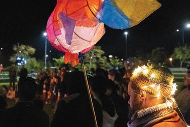 A man with lights on his hat holds a colourful paper lantern fish. 