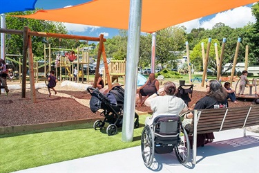 People, including a wheelchair user, watch on as children play at Raumanga Scenic Reserve Playground.