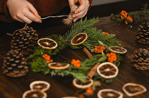 A person creates a natural Christmas wreath decoration with pinecones, branches and dried fruit. 