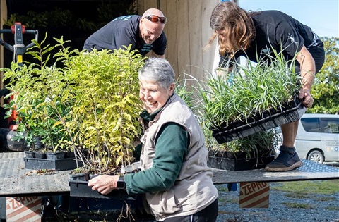 One woman and two men unload native plants from a truck at Botanica.