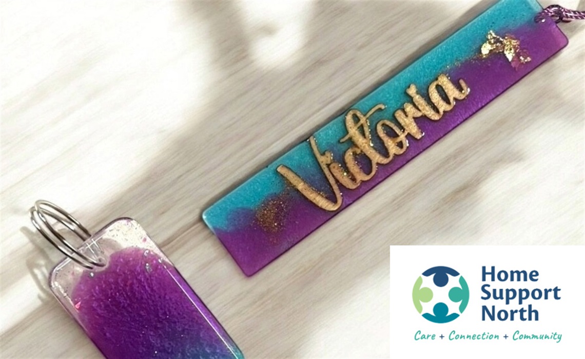 Two colorful resin keychains on a light wooden surface. One says  Two colorful resin keychains on a light wooden surface. One says