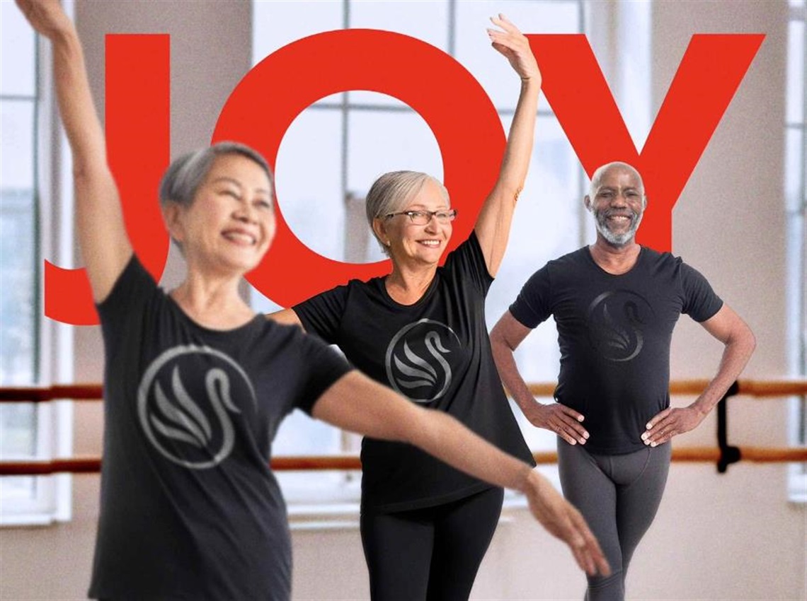 Ballet North promotional image showing three adults in a dance studio wearing black outfits with a swan logo. Large red text saying joy appears behind the dancers.
