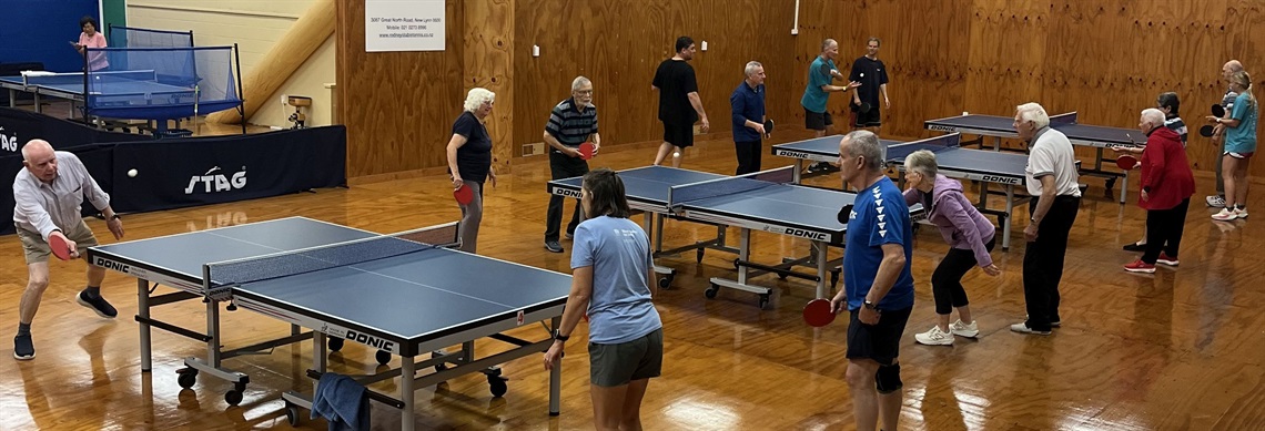Seniors playing table tennis in a hall.