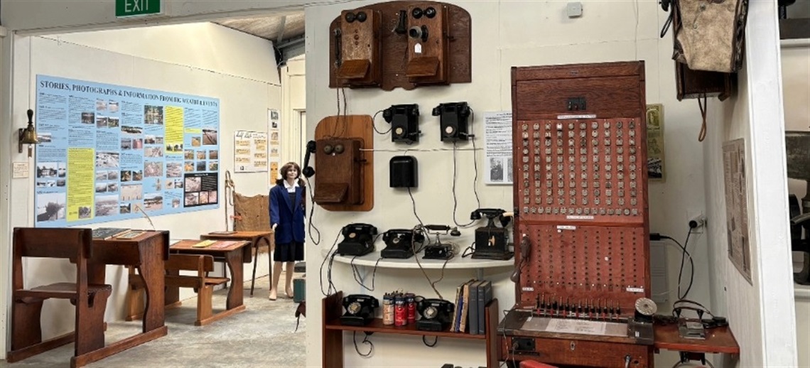 Museum exhibit displaying vintage telecommunication devices including old telephones and a switchboard, with a World War II-themed display board and a mannequin in period clothing in the background.