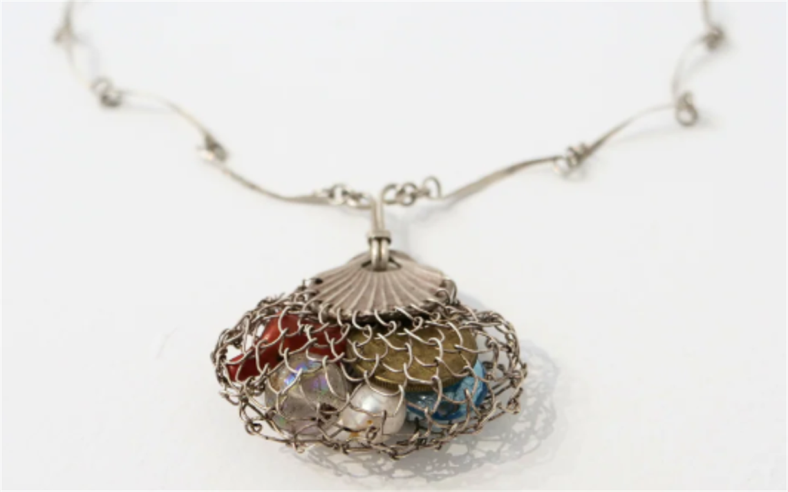 Close-up of a handcrafted necklace featuring a wire mesh pendant filled with colorful beads, including red, blue, and metallic tones. The pendant is attached to a delicate, twisted silver chain with small loops, displayed against a plain white background.