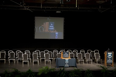 Te Kotahitanga Exhibition Hall audience view of stage with many chairs, tables, and lectern setup.