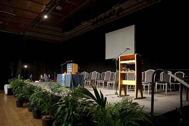 Te Kotahitanga Exhibition Hall stage corner angle with chairs placed on stage with lectern and table.