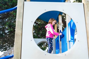 Child playing with steering wheel on play equipment at the playground at Marsden Bay reserve, One Tree Point.