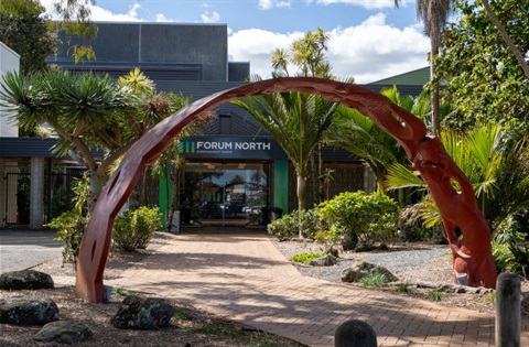 Entrance to Forum North building with a large carved wooden archway surrounded by plants. 