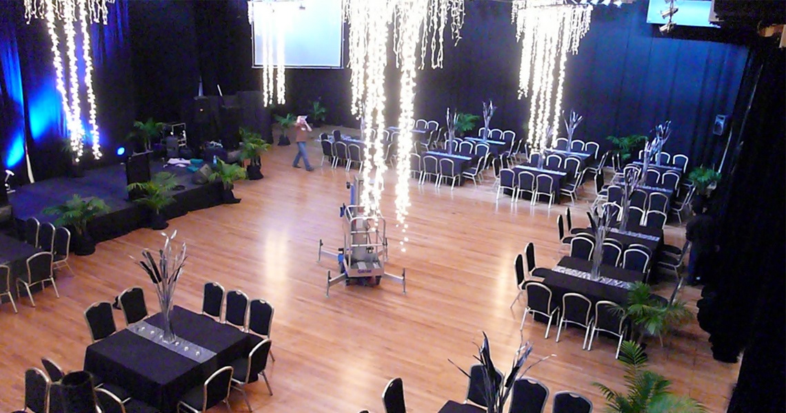 Photo of the Te Kohitanga Exhibition Hall in the cocktail or banquet layout, with stage and lighting from the roof. 