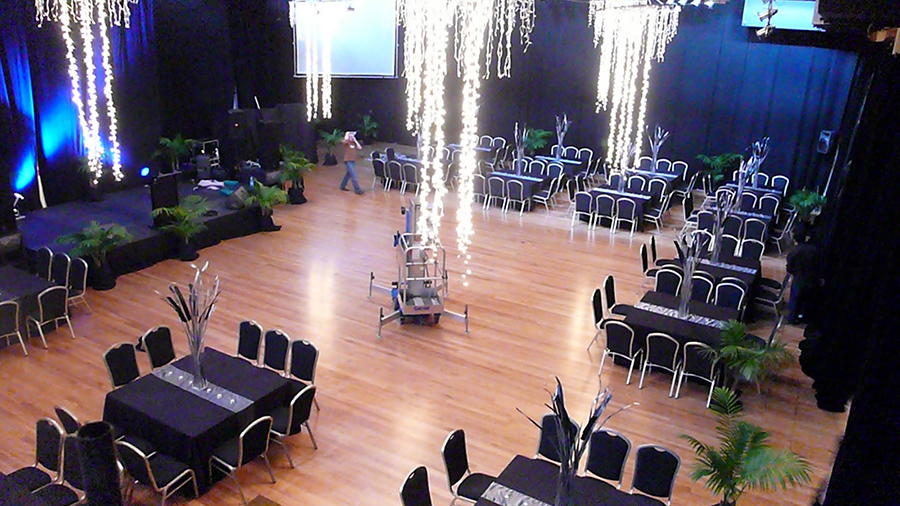 Exhibition Hall cocktail layout, high angle with lights hanging from the ceiling with tables and chairs setup. 