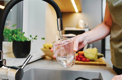 A person filling a glass of water from a kitchen tap. 